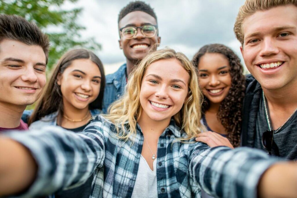 A group of smiling teens pictured in a self portrait taken at a community event outdoors.