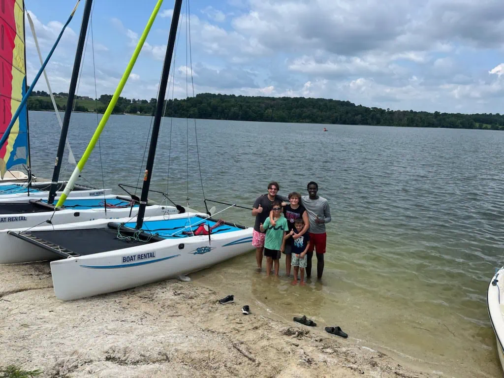 Group posing by rented boats on lake shore.